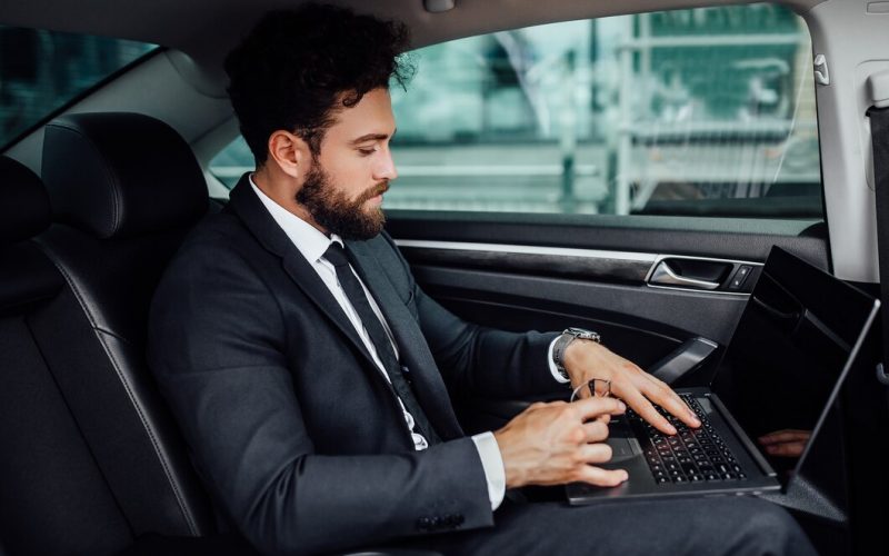 handsome-bearded-smiling-top-manager-black-suit-working-his-laptop-backseat-car_496169-590